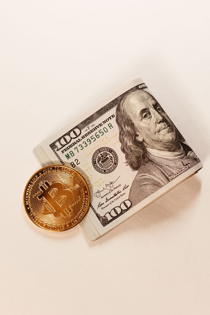 Mastering the First Impression: Your intriguing post title goes here Close-up of a Bitcoin coin placed beside a stack of $100 US dollar bills, showcasing cryptocurrency and traditional currency.