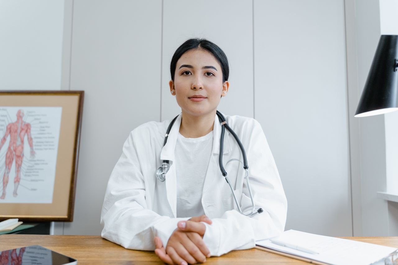 creative-03 Young female doctor sitting at desk with stethoscope, ready for telehealth consultation.