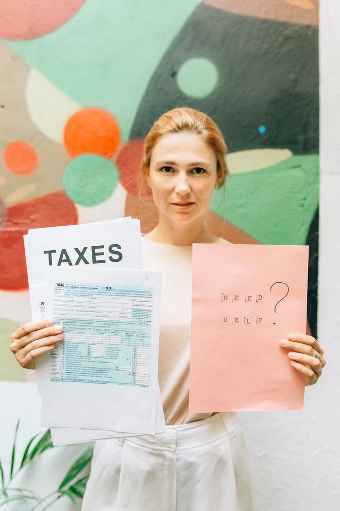 why-choose-us A professional woman holding tax documents and a 'Need Help?' sign, offering tax assistance.
