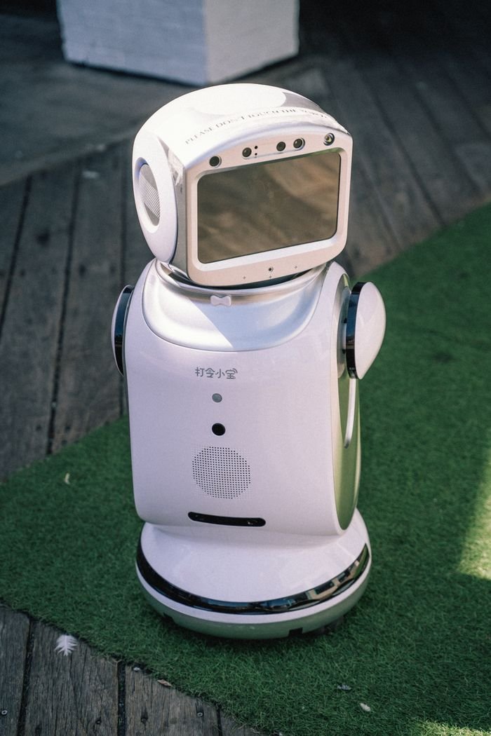 creative-03 A modern robot stands on grass and wooden flooring, showcasing cutting-edge technology.